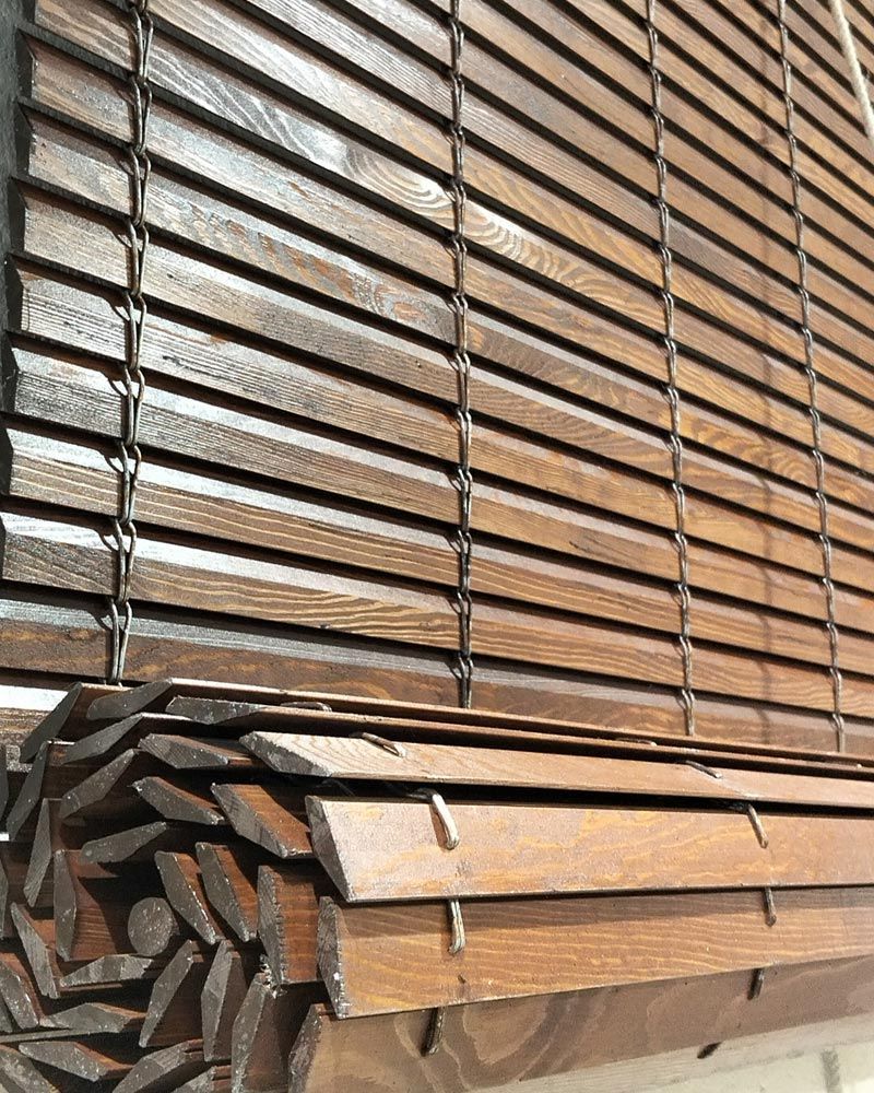 Listones de madera apilados y tablones agrupados, apoyados verticalmente contra una pared, en tonos marrones.