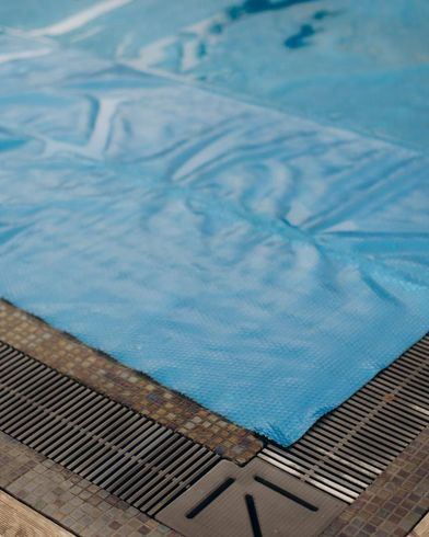Una lona azul para piscina se extiende sobre un desagüe de esquina y una rejilla.
