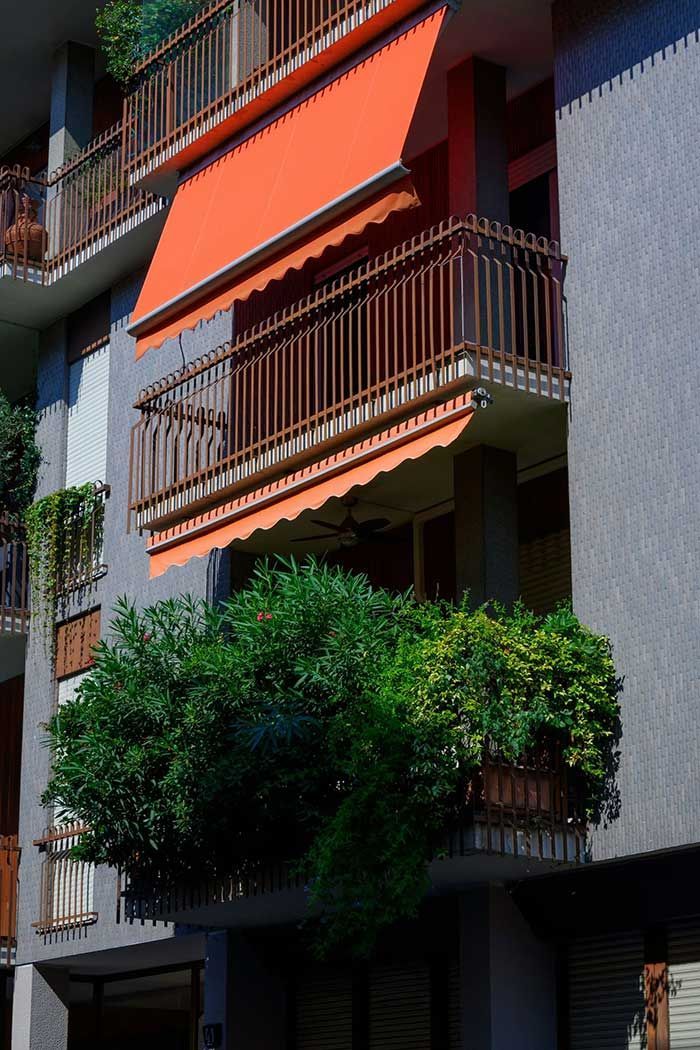 Balcones con toldos naranjas y exuberantes plantas verdes en la fachada gris de un edificio de apartamentos