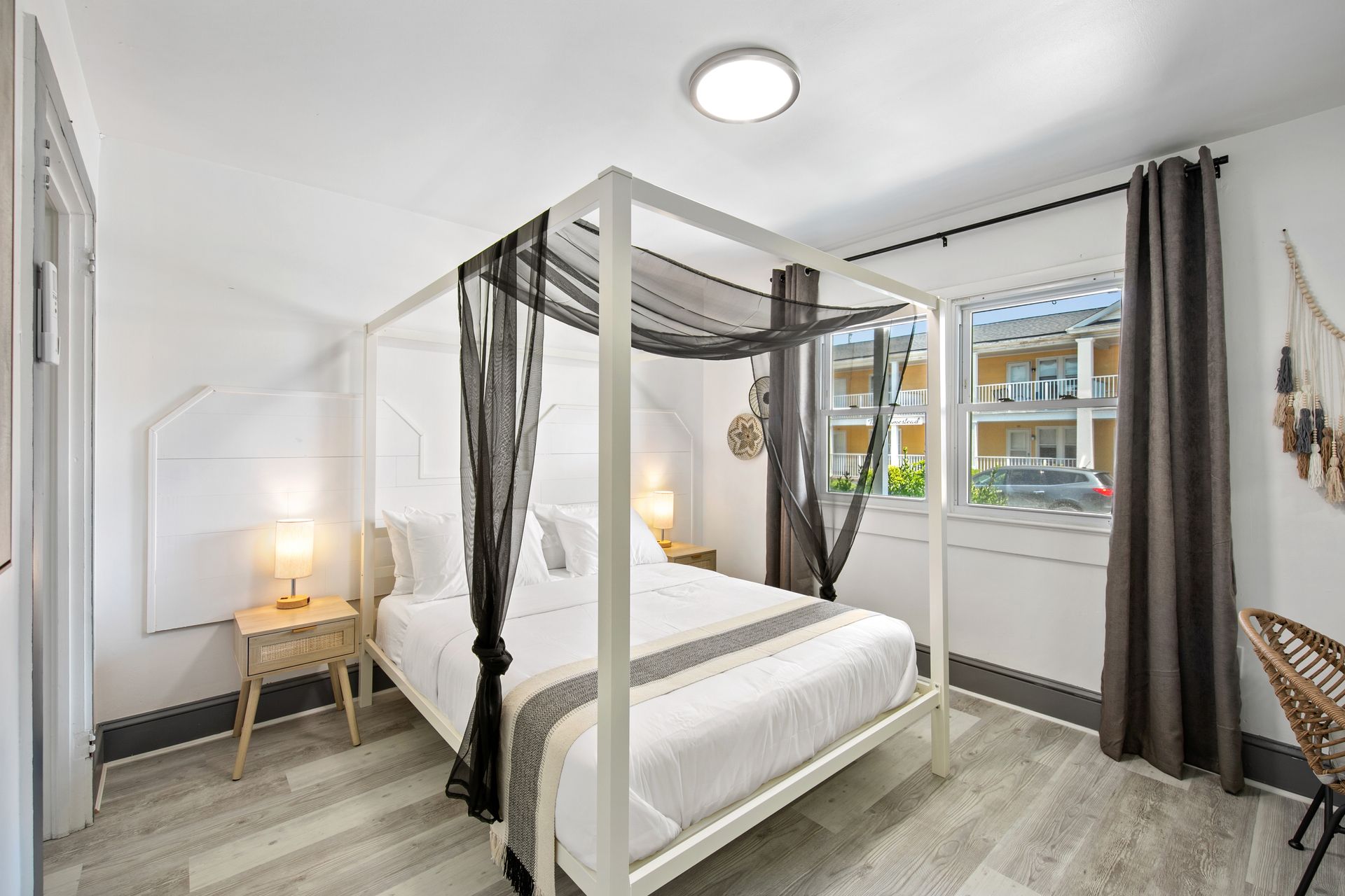 Bedroom with white canopy bed, gray curtains, wood floor, and side table.