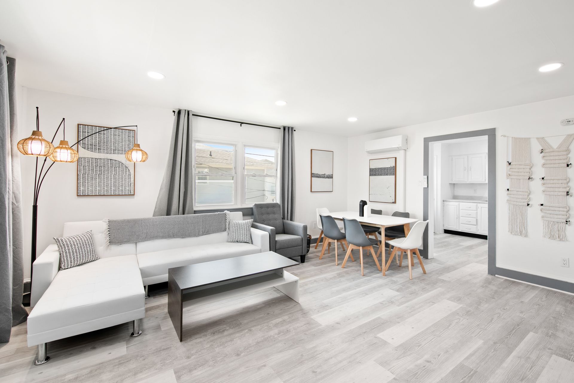 Modern open-concept living space with white walls, light gray flooring, and a dining area.