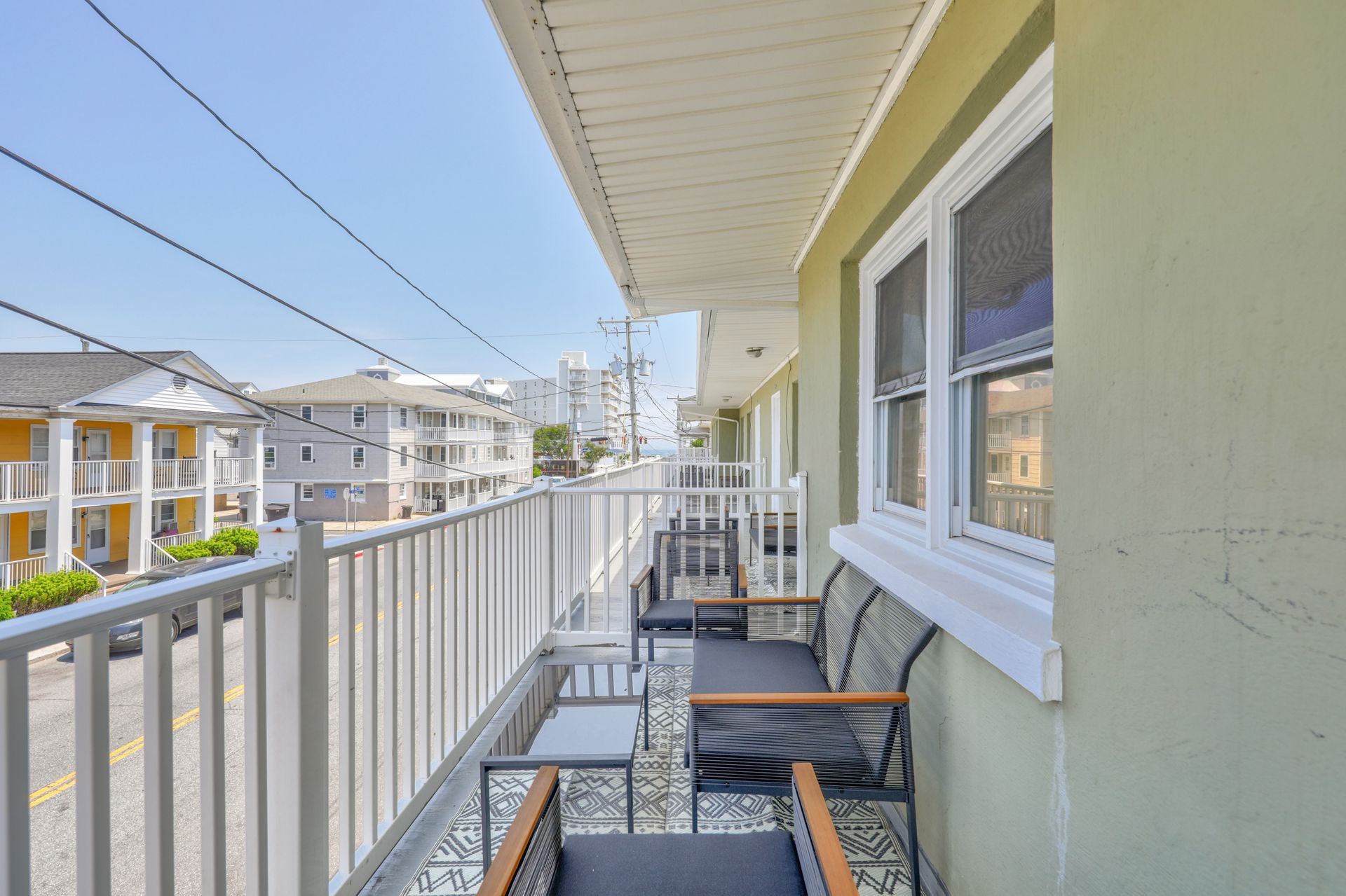 Balcony with seating, overlooking street with buildings and blue sky.
