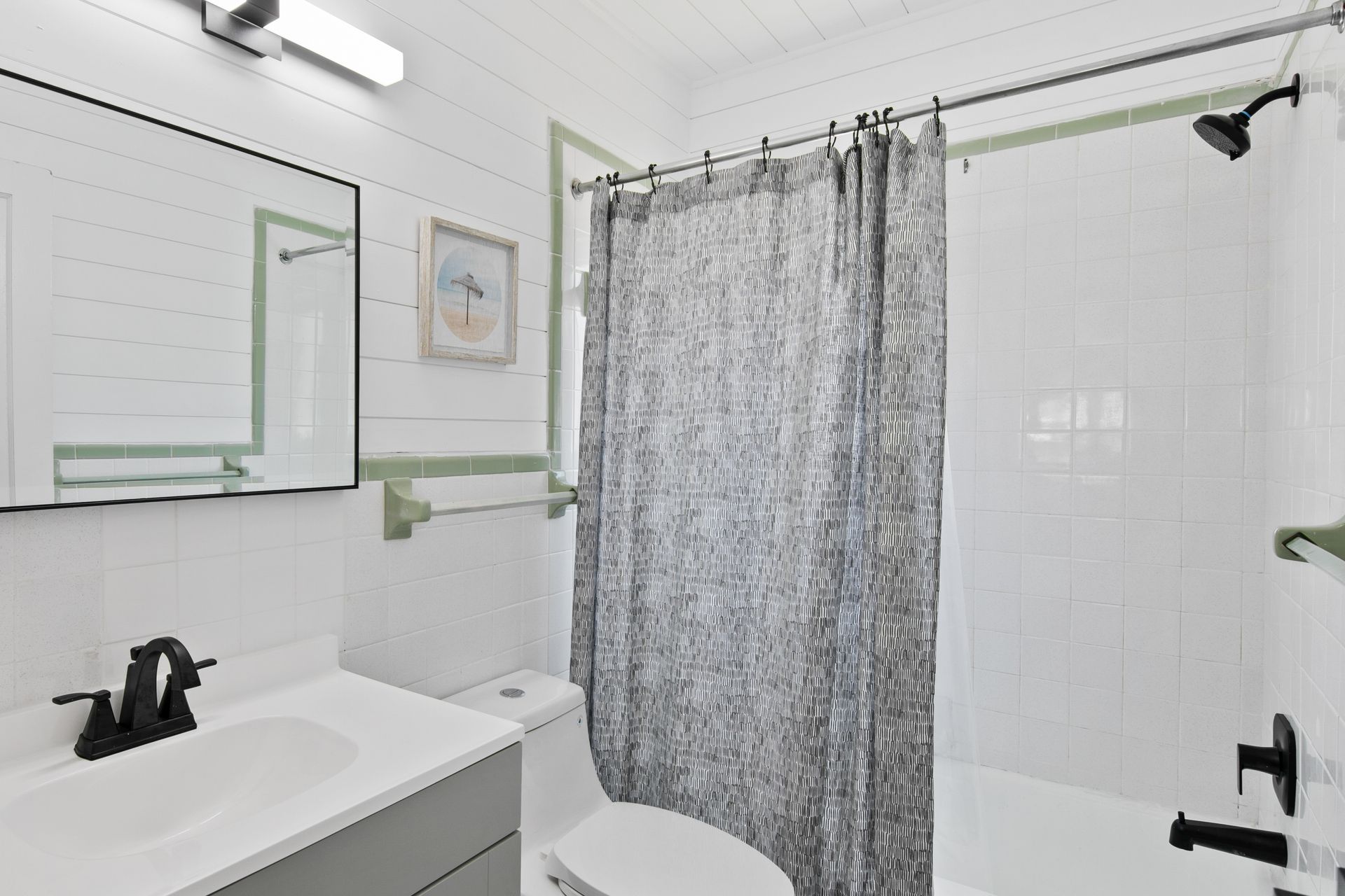 Bathroom with white walls, gray vanity, and black fixtures. Shower has a gray patterned curtain.