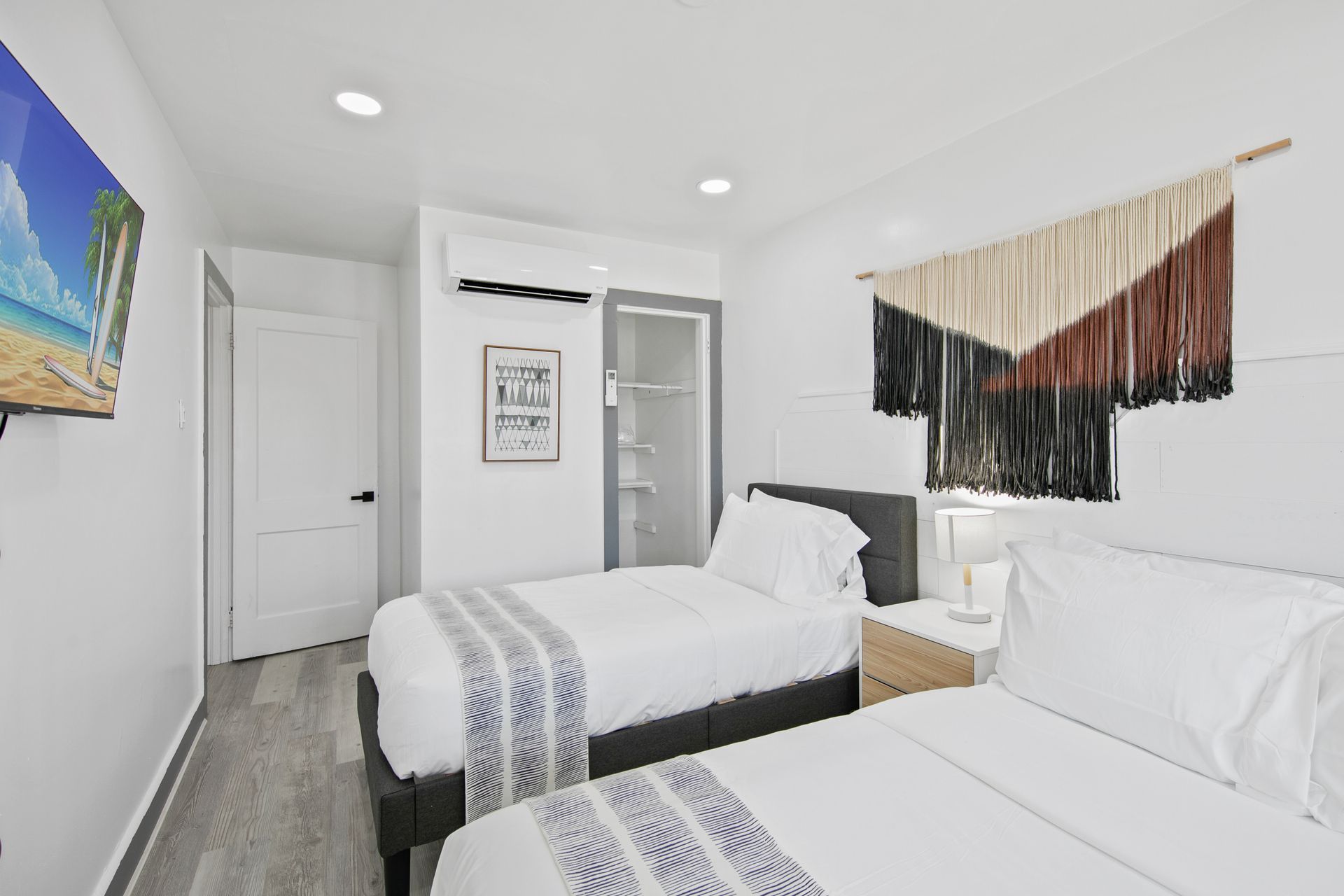 Bedroom with two twin beds, white walls, gray floors, art and a wall hanging.
