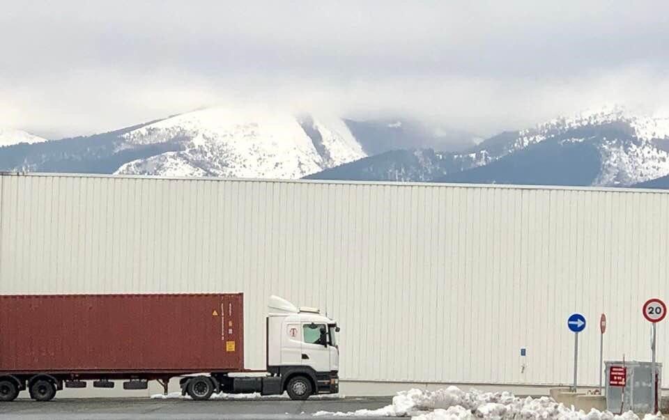 Un camión está estacionado frente a un edificio con montañas al fondo.