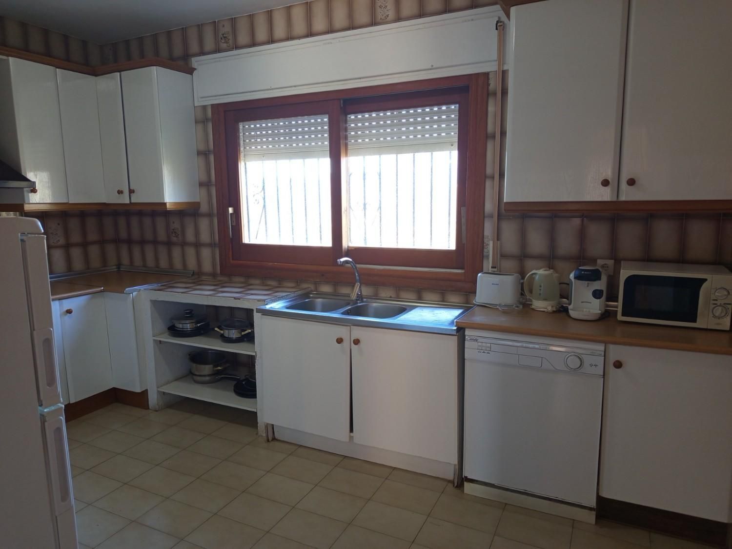 Una cocina con armarios blancos, una ventana sobre el fregadero, lavavajillas, microondas y salpicadero de azulejos.