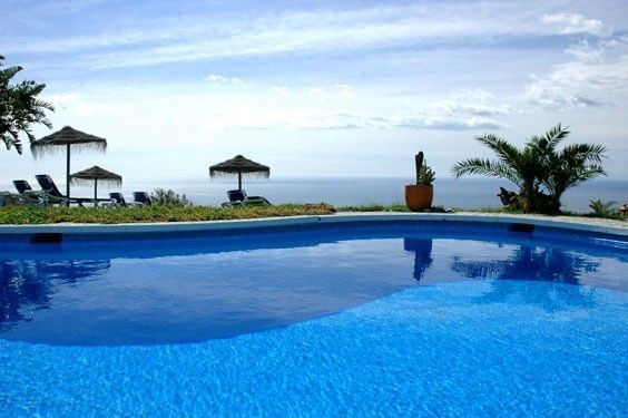 Una piscina de color azul brillante tiene vistas al océano, con sombrillas de paja