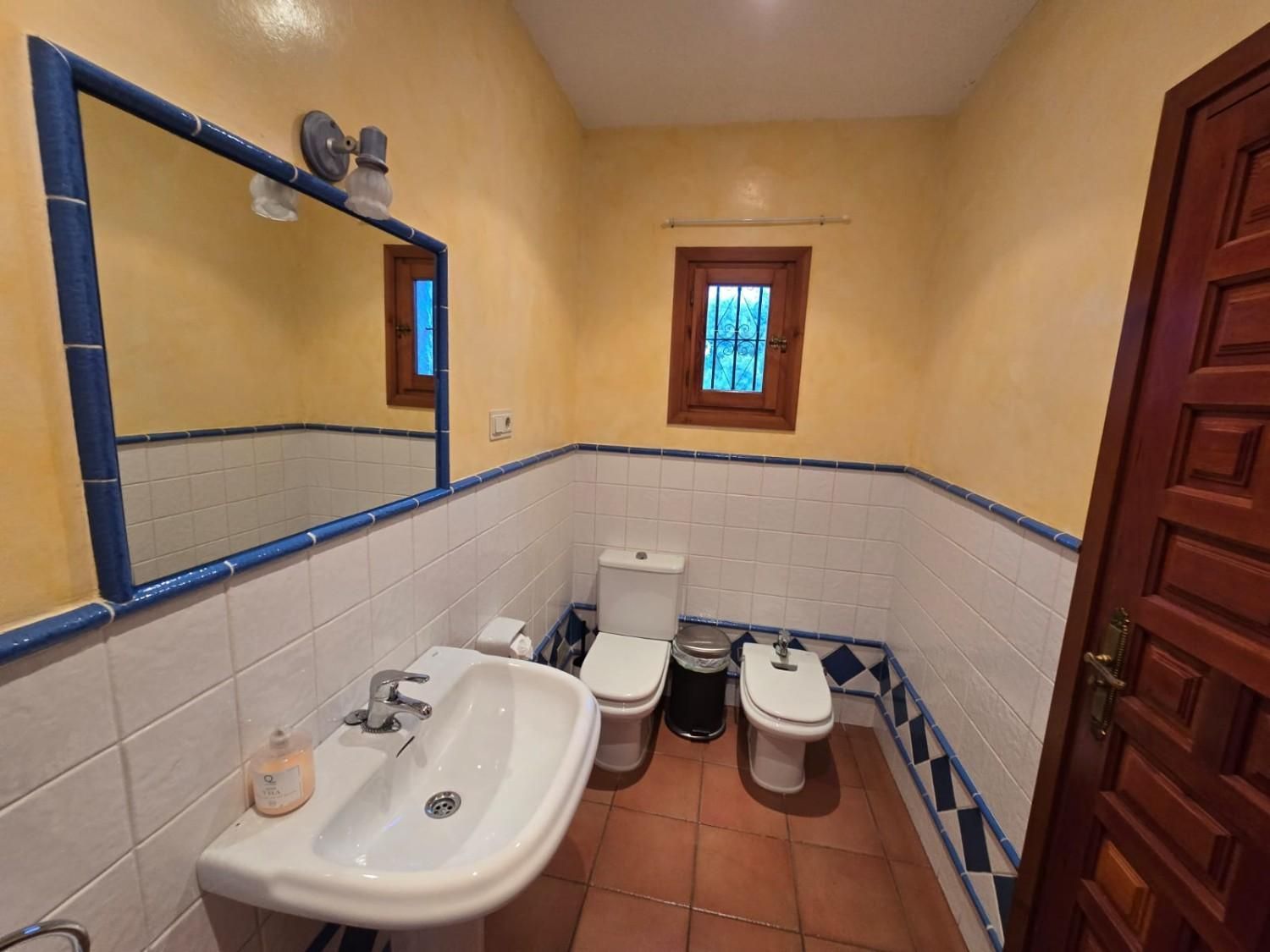 Un baño con paredes amarillas, revestimiento de azulejos blancos
