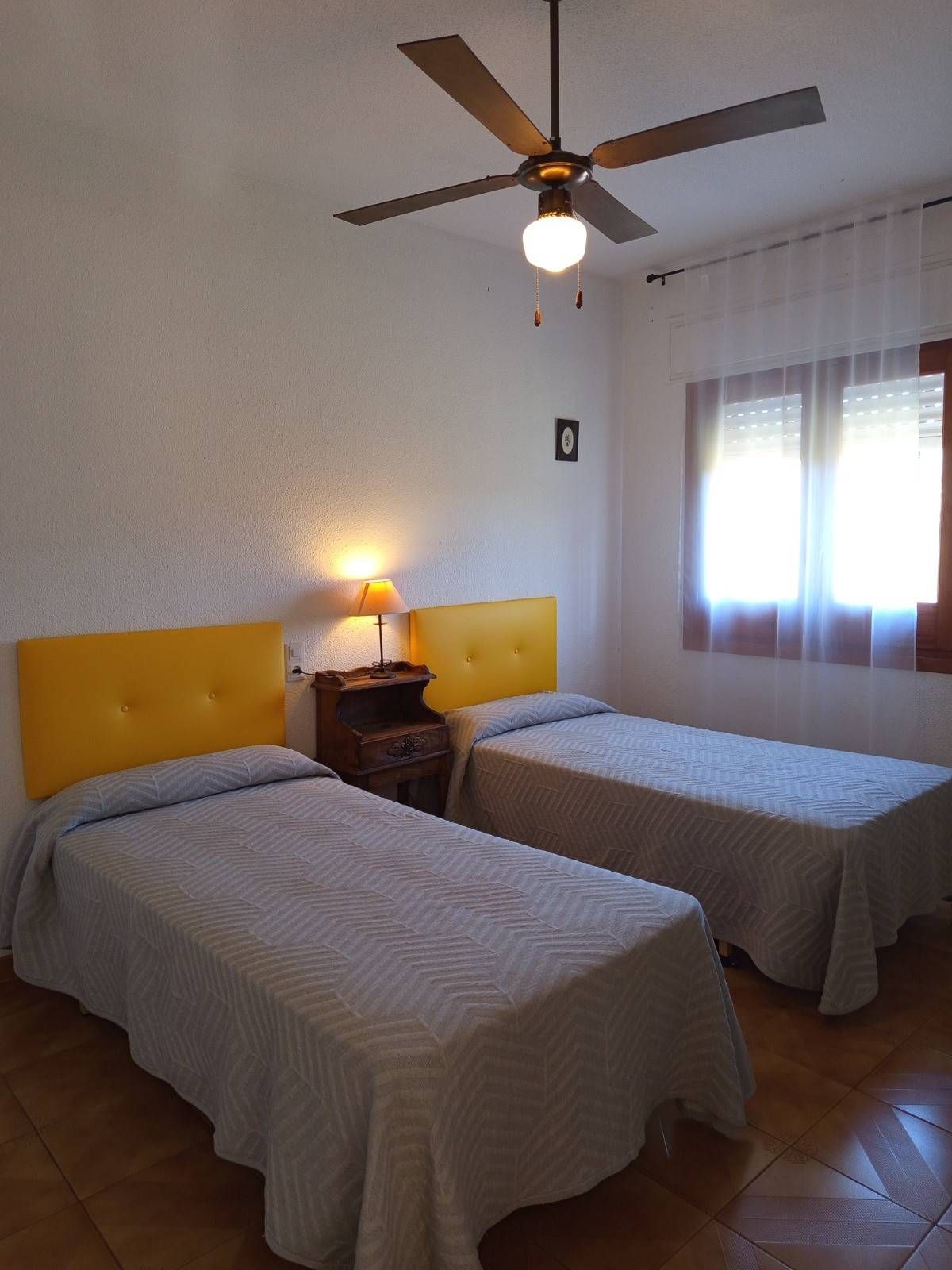 Un dormitorio con dos camas individuales con cabeceros de color amarillo brillante, colchas a juego y un ventilador de techo.