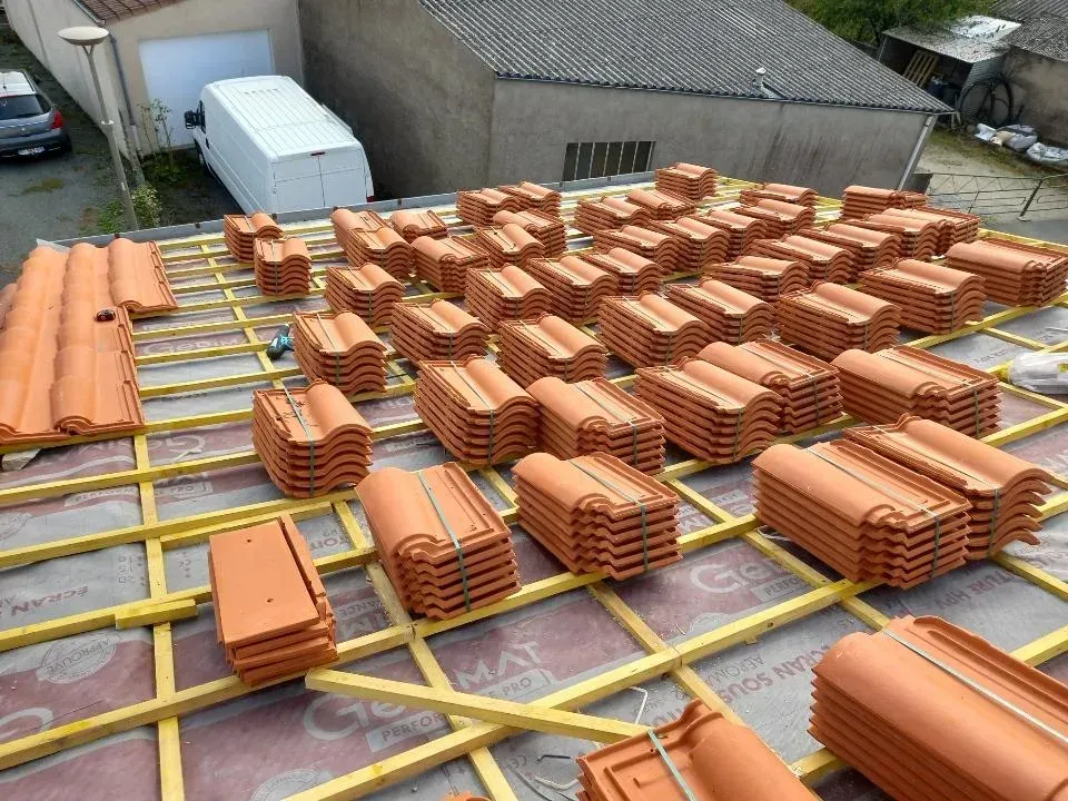 Toiture avec des piles organisées de tuiles en terre cuite orange prêtes à être installées.