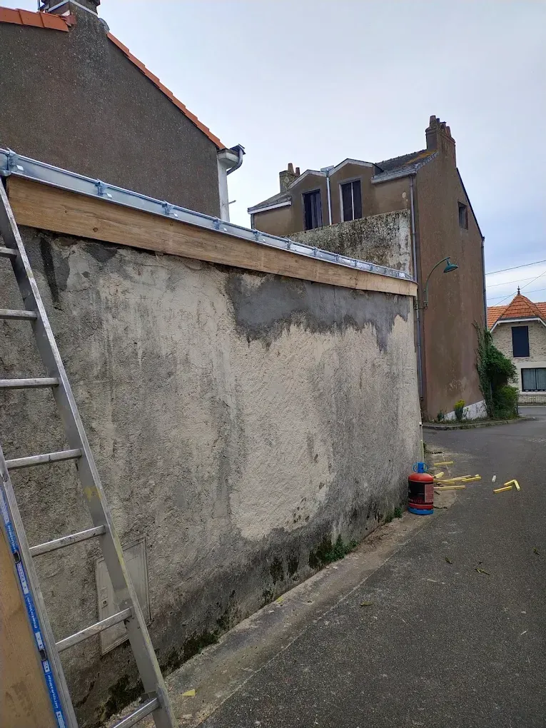 Échelle adossée à un mur en stuc, avec une nouvelle charpente en bois et une bande métallique en partie supérieure.