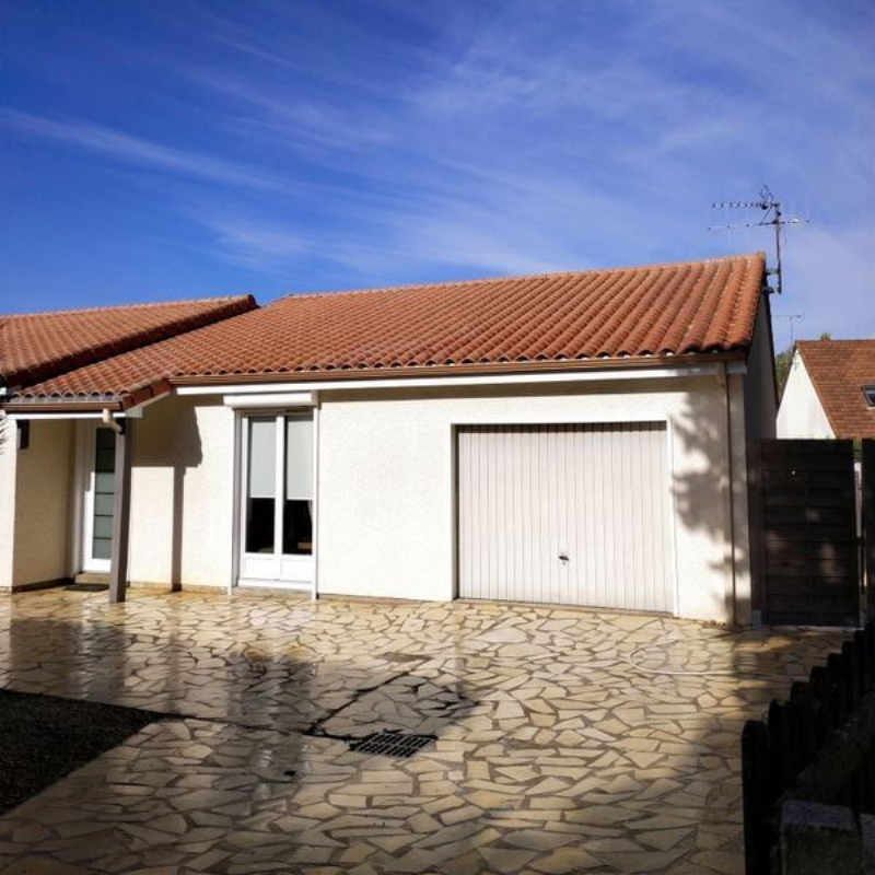 Maison blanche au toit de tuiles rouges, porte de garage blanche et allée en pierre sous un ciel bleu.