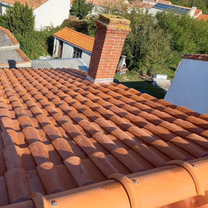 Toit de tuiles rouges avec cheminée en briques, scène extérieure ensoleillée.
