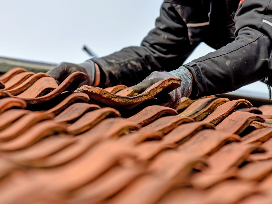 Personne portant des gants installant des tuiles de toit en terre cuite rouge.