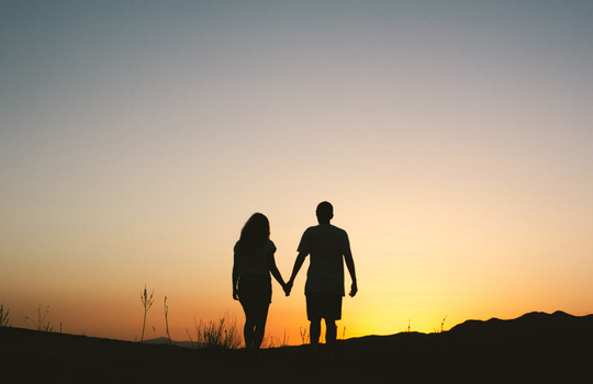 Couple se tenant la main devant un coucher de soleil