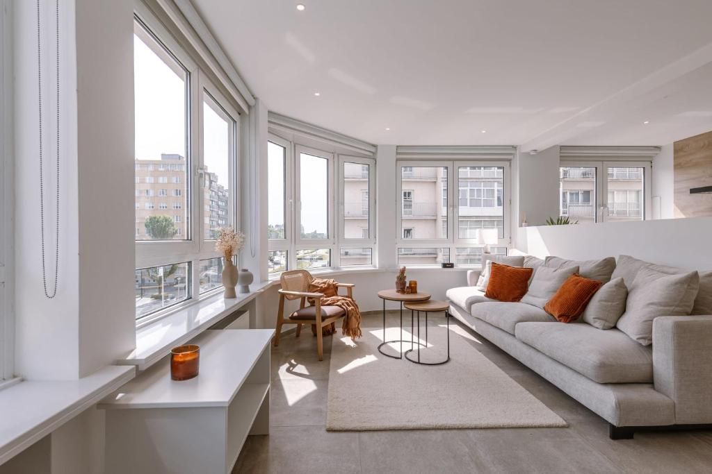 Bright living room with large windows, beige sofa, orange pillows, and a rug.