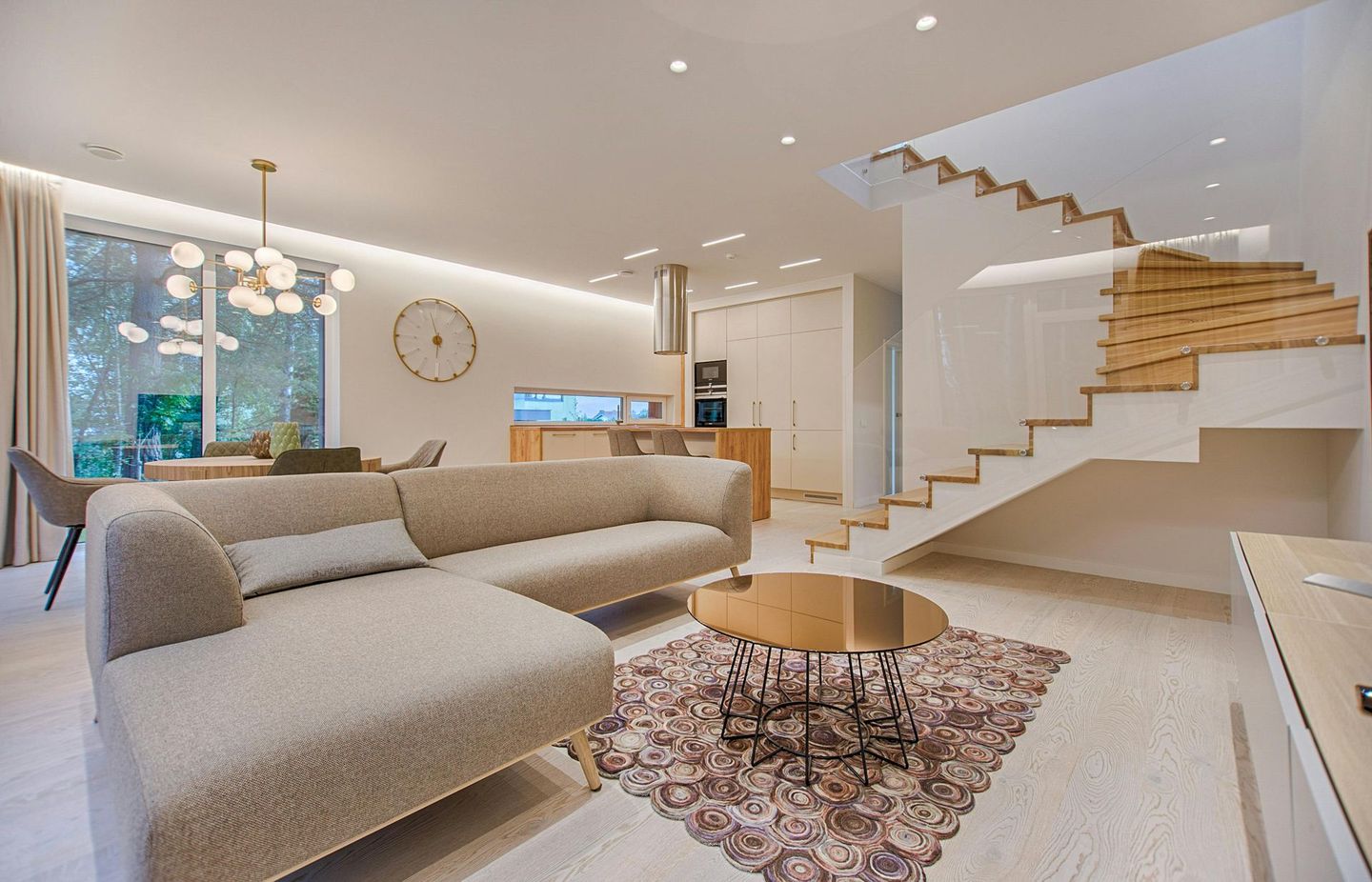 Modern living room with staircase, beige sofa, and coffee table on floral rug.