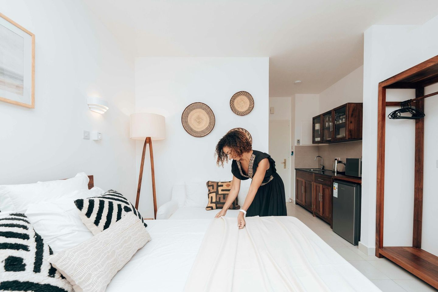 Woman making bed in a bright white room with minimalist decor.