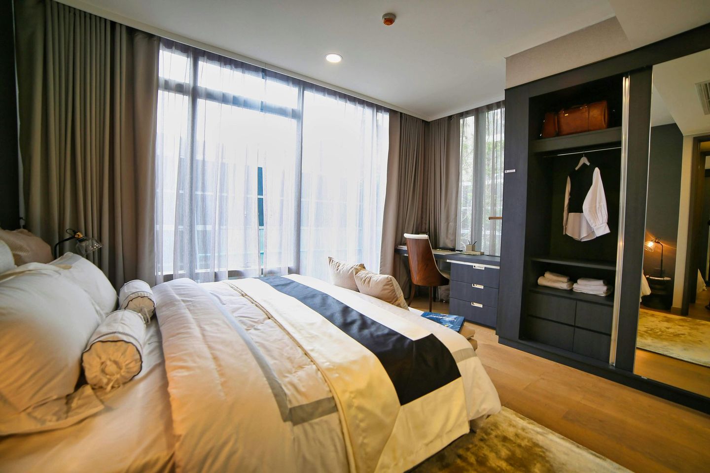 Bedroom with large bed, closet, desk, window. Neutral colors, soft lighting.