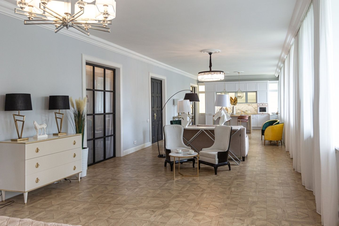 Spacious light-blue room with white furniture. Includes lamps, table, chairs, and a chandelier.