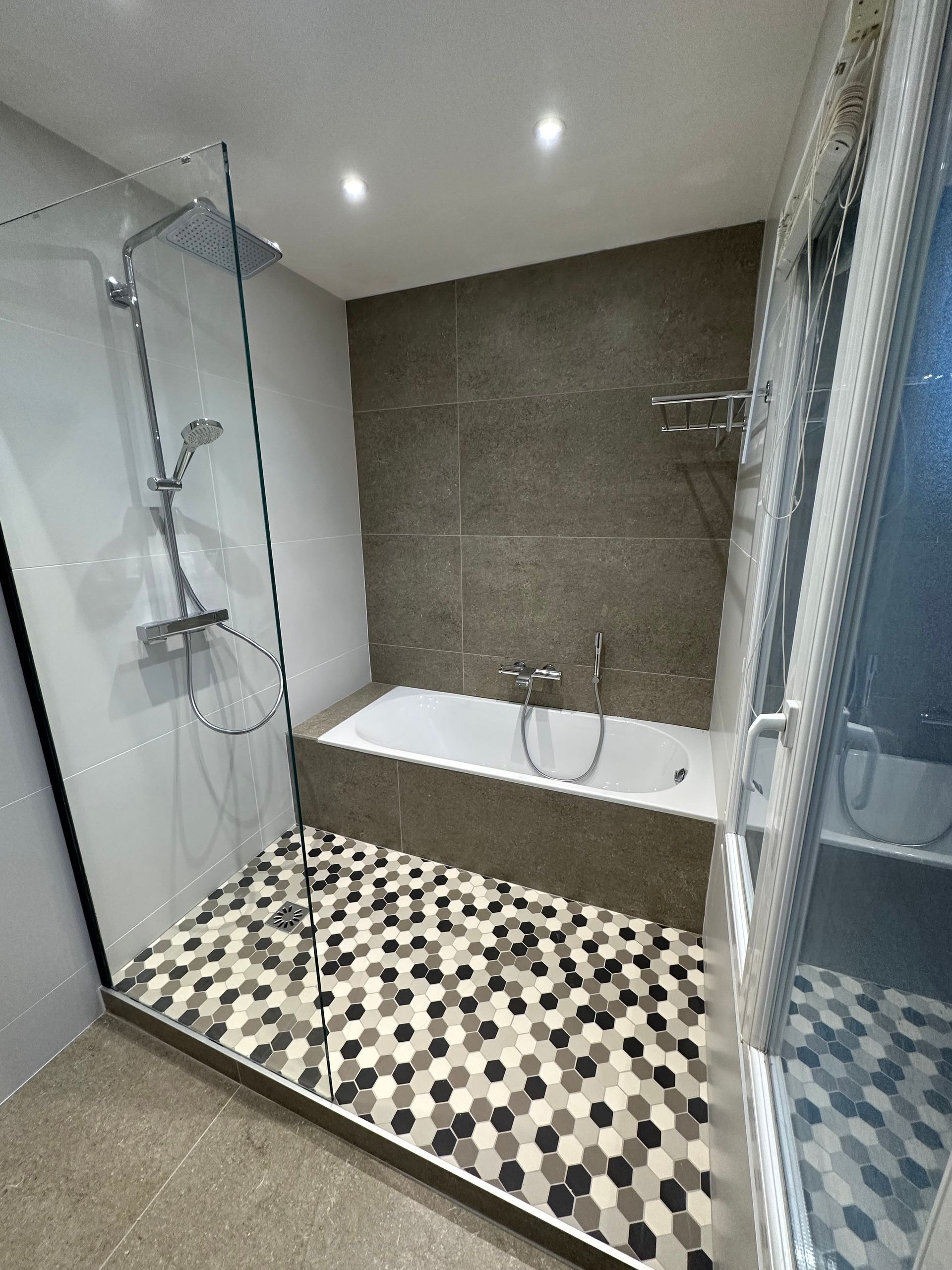 Baignoire grise derrière une douche à l'italienne avec un motif à hexagone
