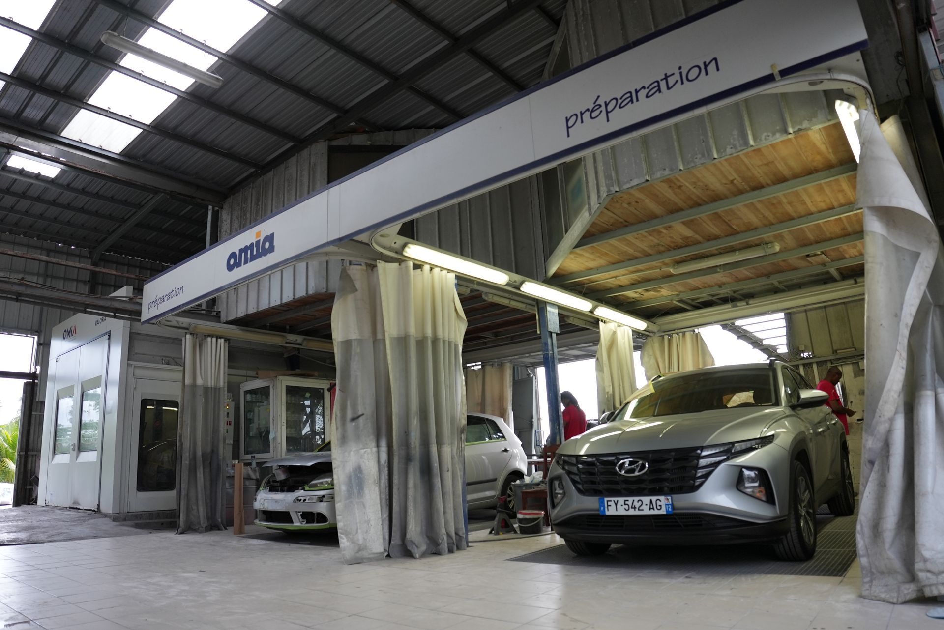 Voitures dans un hangar d'inspection couvert, avec rideaux et éclairage zénithal puissant.