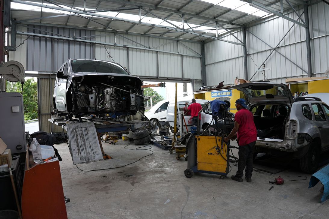 Atelier de réparation automobile avec un bus sur un pont élévateur et un mécanicien travaillant à côté d'une charrette à outils jaune