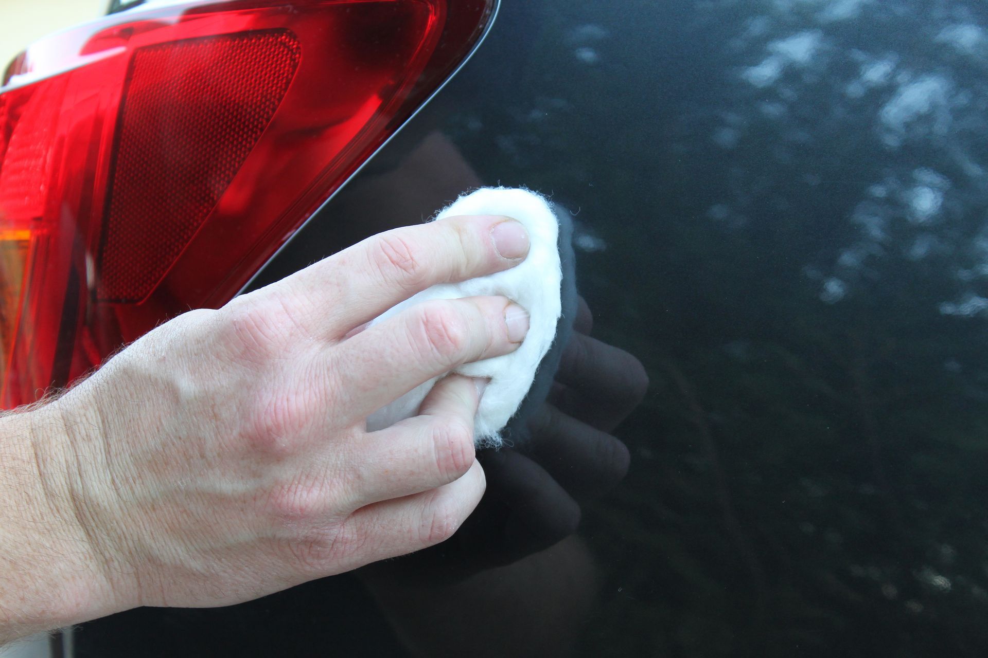 Essuyer à la main l'arrière d'une voiture noire avec un chiffon blanc près d'un feu arrière rouge