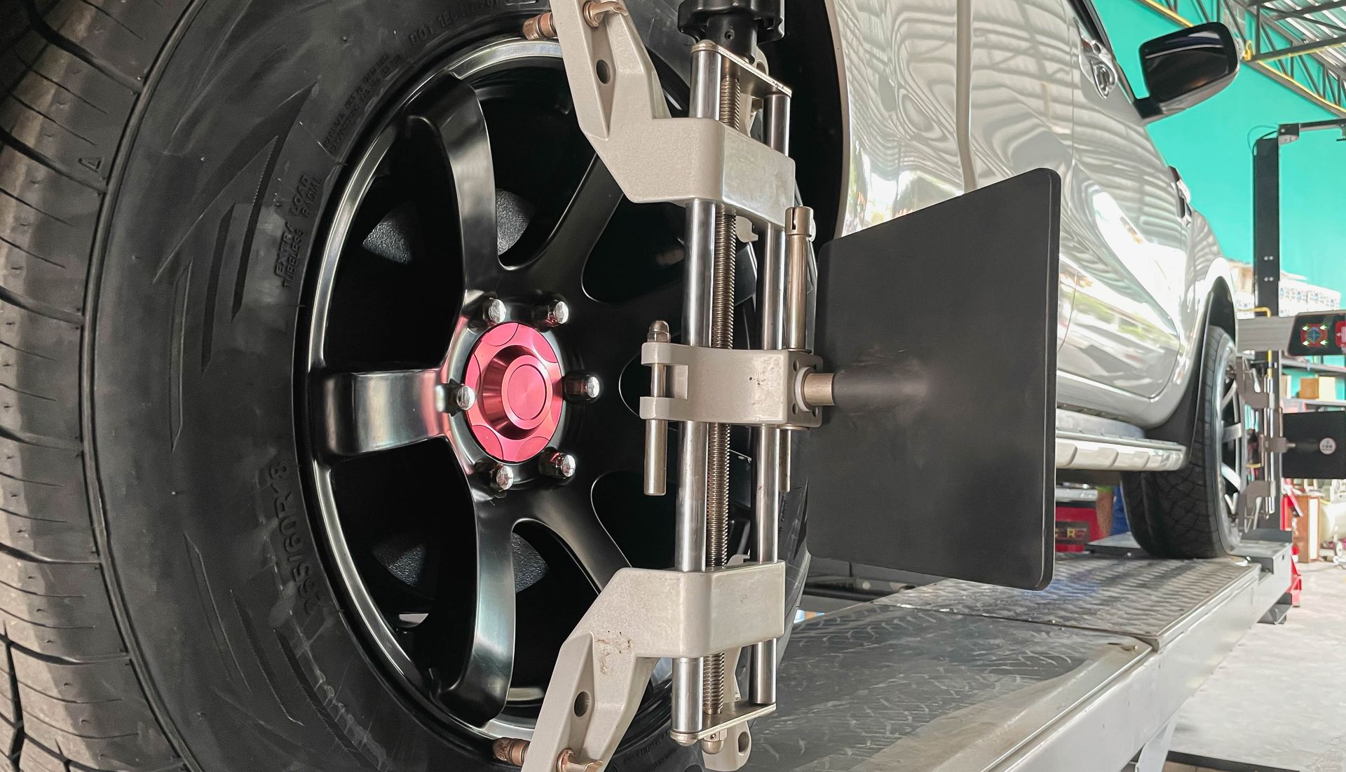 Gros plan sur une roue de voiture de course noire avec un moyeu rose et du matériel de changement de pneu dans un garage