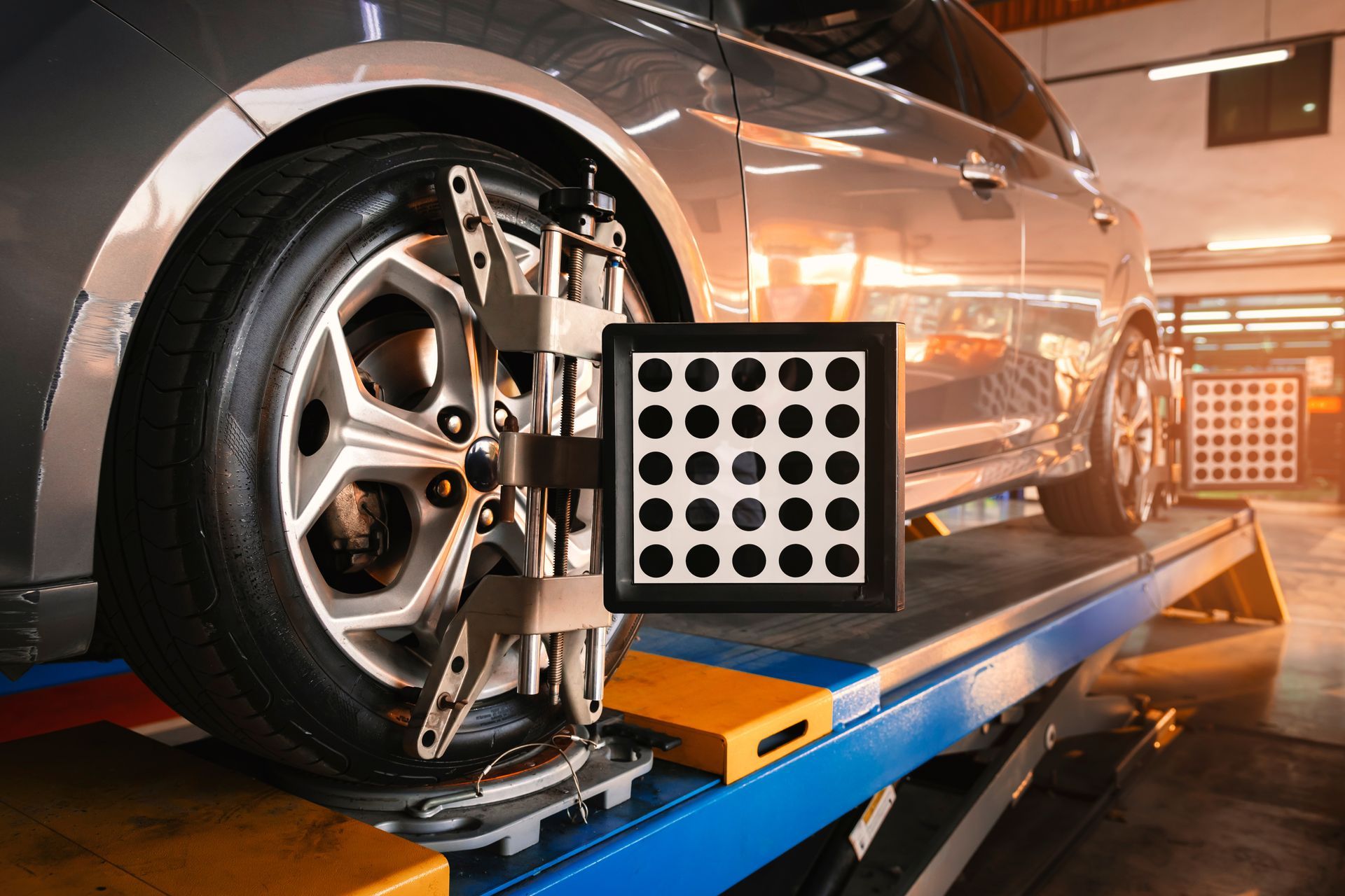 Voiture sur une machine d'alignement des roues dans un atelier de réparation automobile, avec une cible de calibration à côté de la roue avant