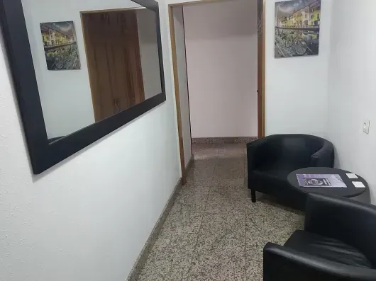 Un pasillo con dos sillas y un espejo en la pared.