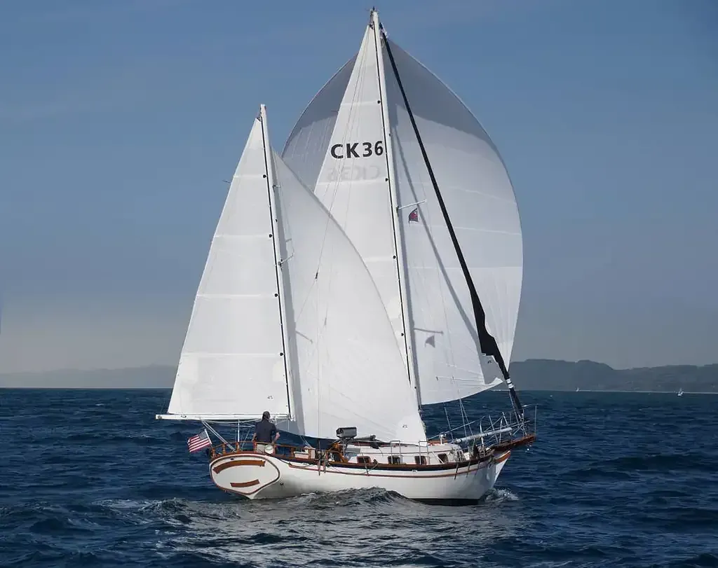 Barco de vela con velas blancas sobre agua azul, bajo un cielo despejado.