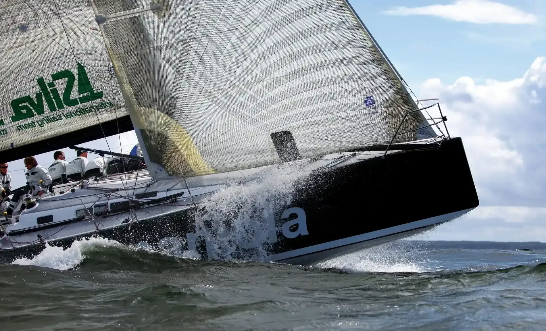 Velero corriendo en el agua, casco negro, velas blancas, olas salpicando, equipo en cubierta.