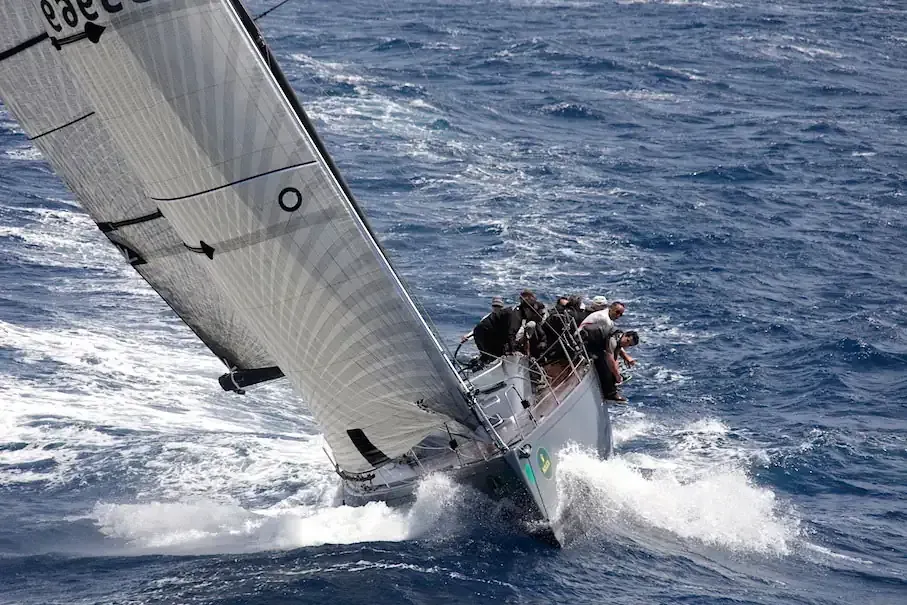 Velero navegando en mares agitados, en un ángulo pronunciado y con la tripulación visible.