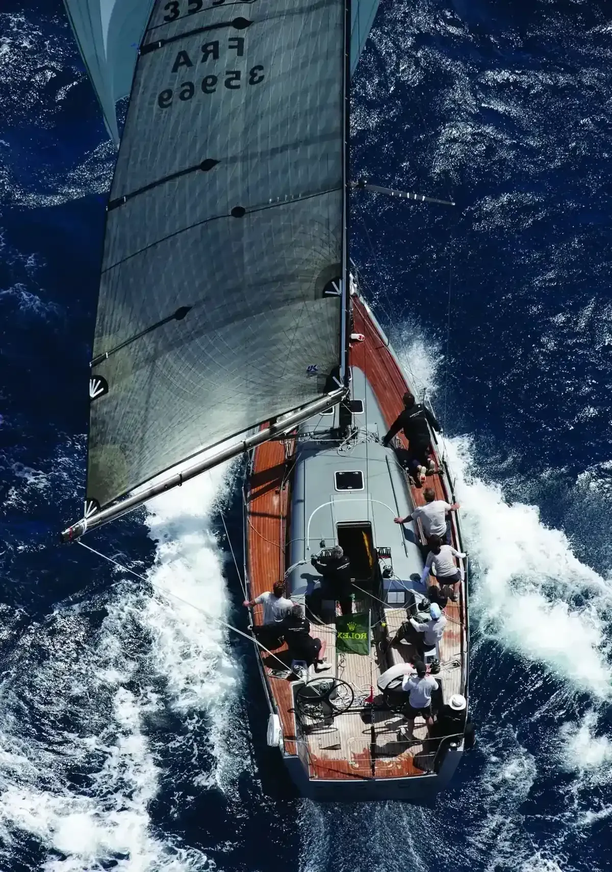 Velero corriendo en aguas azules agitadas; tripulación inclinándose para equilibrar el barco.