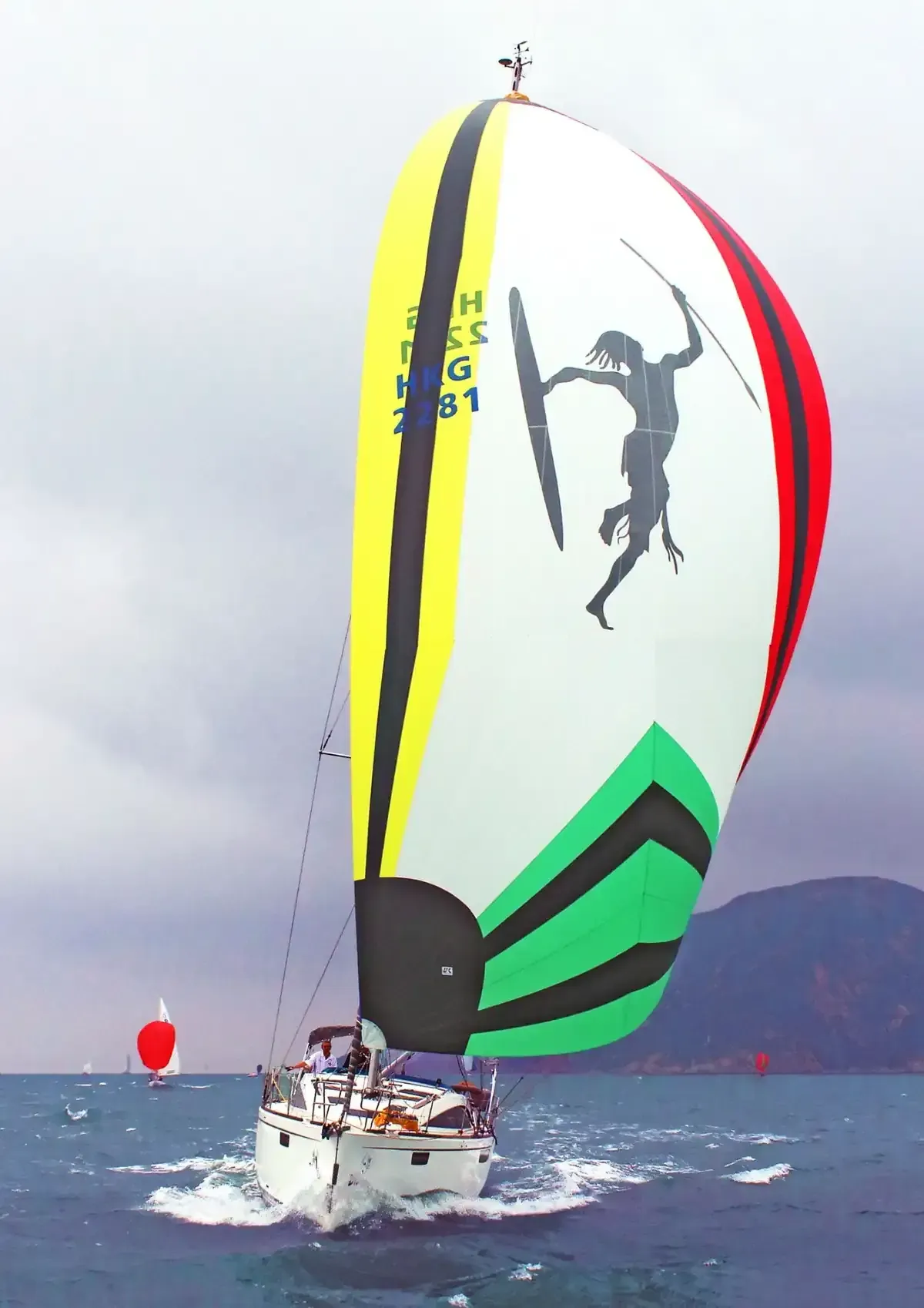 Velero con vela spinnaker de colores, arte indígena, compitiendo en el agua.