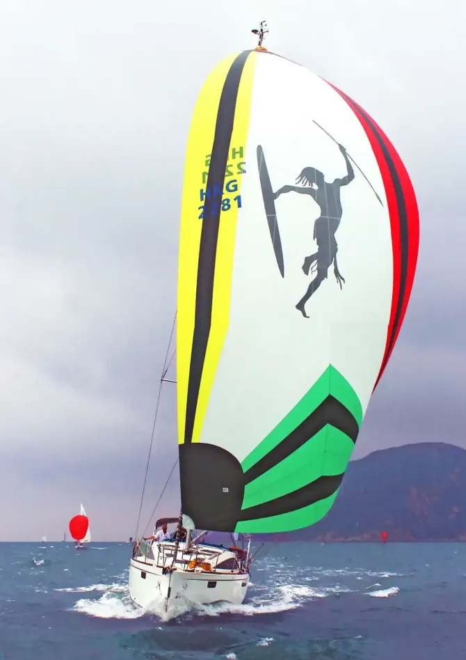 Velero con vela spinnaker de colores, arte indígena, compitiendo en el agua.