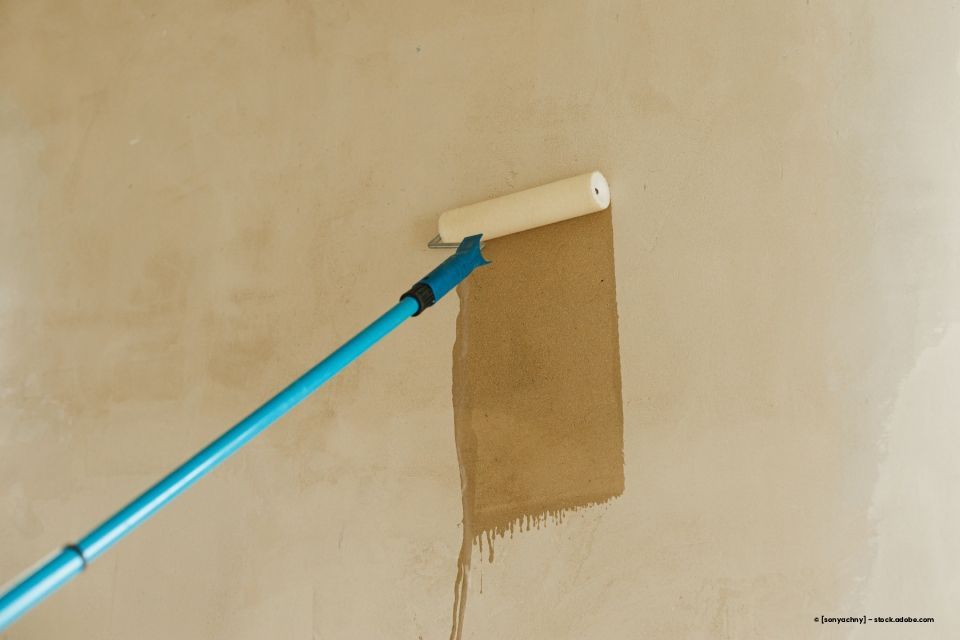 Farbroller zum Auftragen brauner Farbe auf eine beige Wand.
