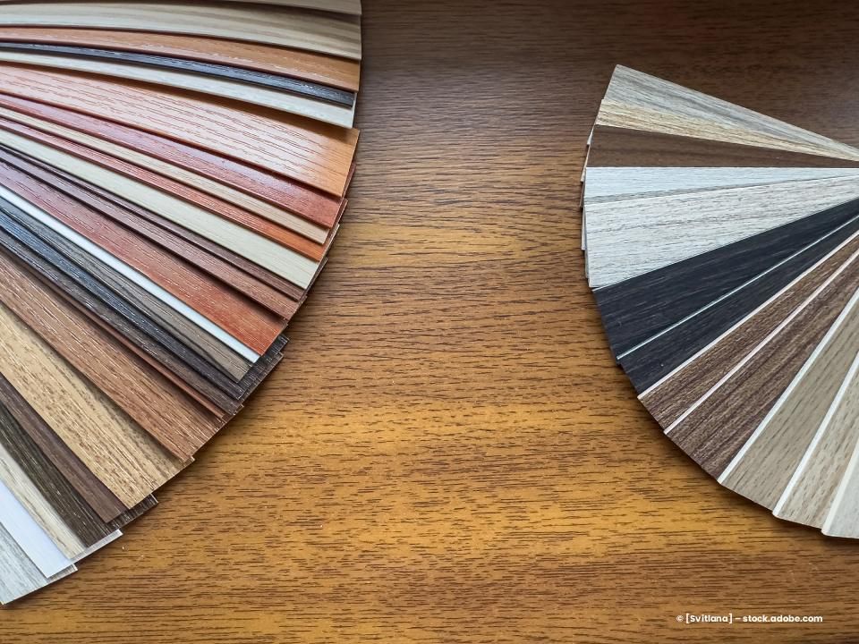 Zwei fächerförmig angeordnete Farbmuster aus Holzfurnier auf einer Oberfläche mit Holzmaserung.