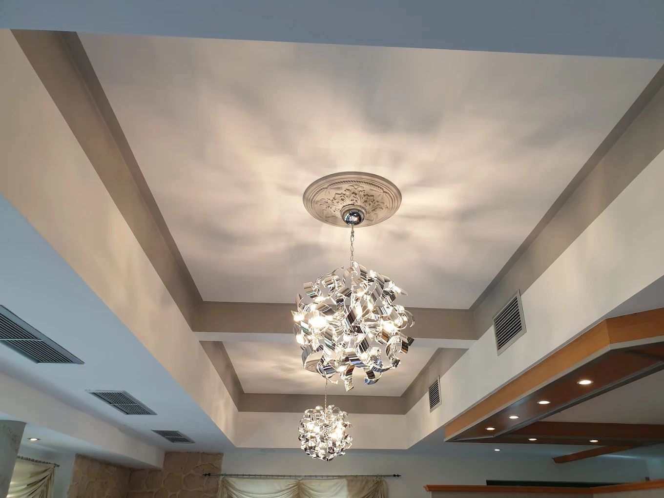 Weiße Decke mit Einbaustrahlern. Zwei hängende, verchromte Kugelleuchter. Graue Akzente.