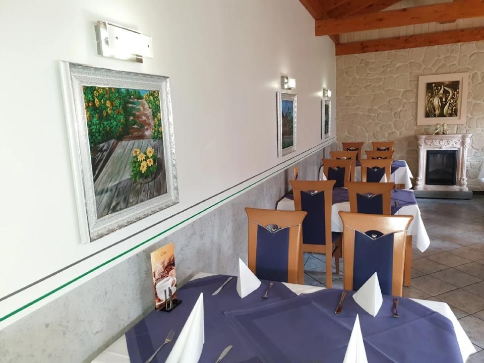 Restaurantinterieur mit gedeckten Tischen, Gemälden an der Wand und einem Kamin.