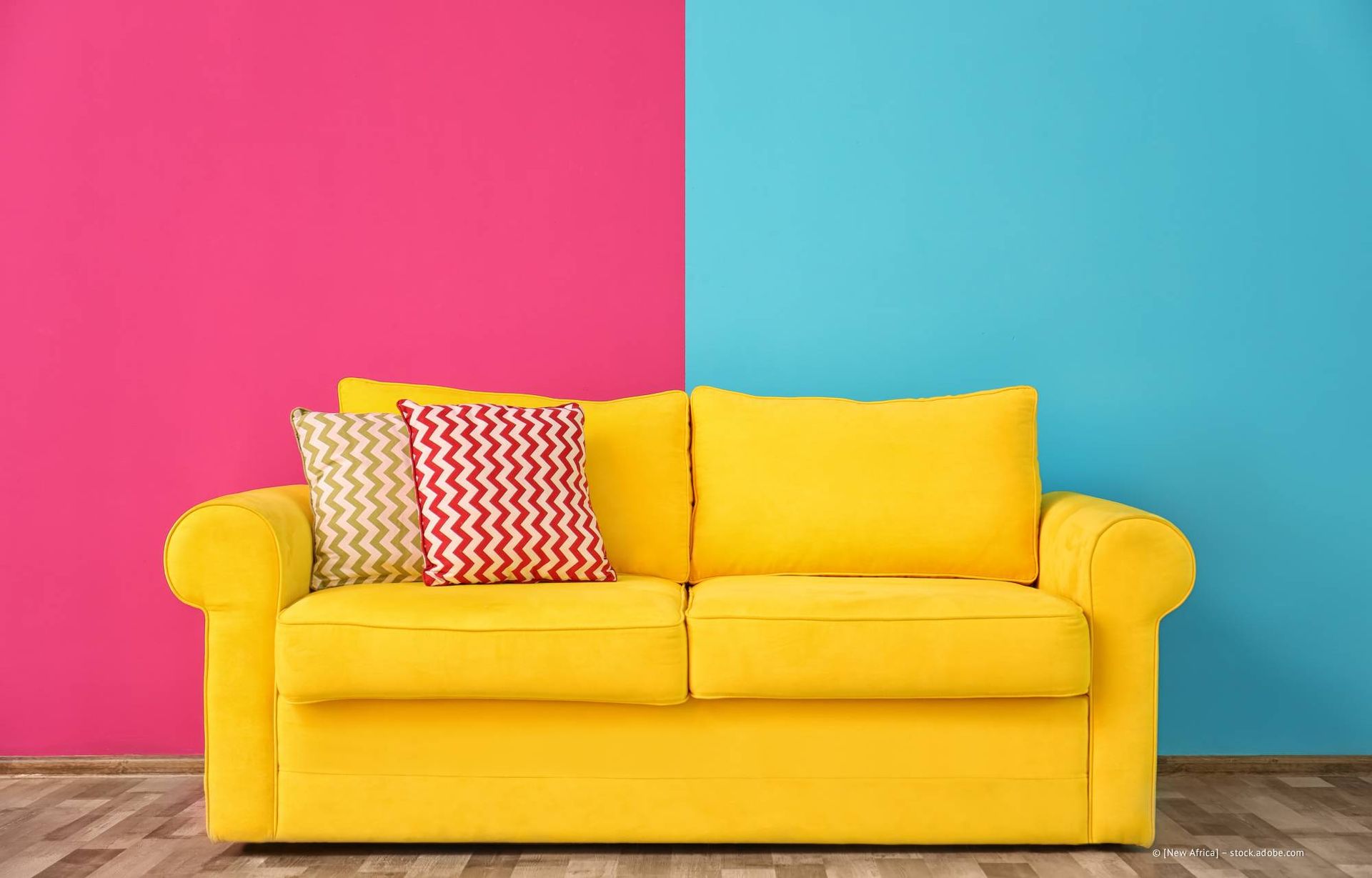 Gelbes Sofa mit zwei Kissen vor einer zweifarbigen Wand in Rosa und Blau.