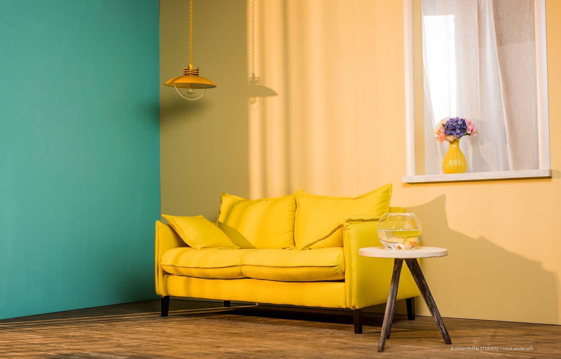 Gelbes Sofa in einem Zimmer mit türkisfarbenen und gelben Wänden, einem Fenster und einer Hängelampe.