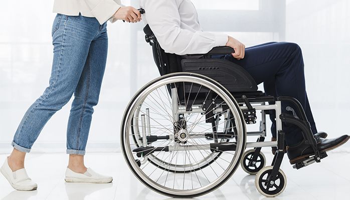 Une femme se tient debout à côté d'un homme en fauteuil roulant.