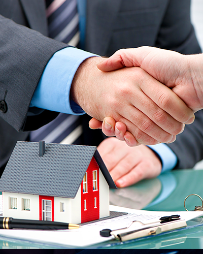 Un homme en costume serre la main d'un autre homme devant une maison modèle