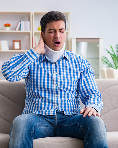 Un homme portant une minerve est assis sur un canapé.