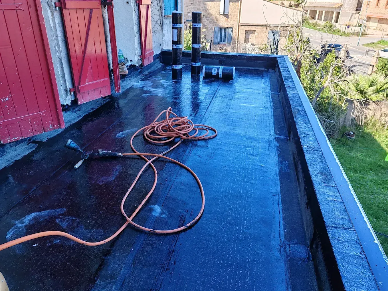 Un toit plat en construction, avec une membrane d'étanchéité noire, des rouleaux de matériau et un tuyau orange en surface.
