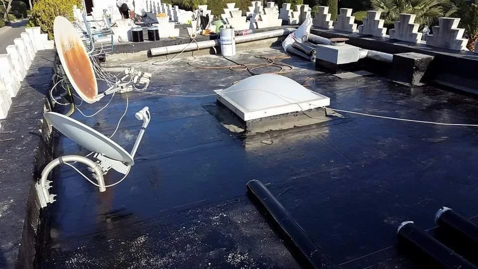 Une surface plane au toit noir, comportant deux antennes paraboliques, un puits de lumière et plusieurs structures blanches fixées au mur.