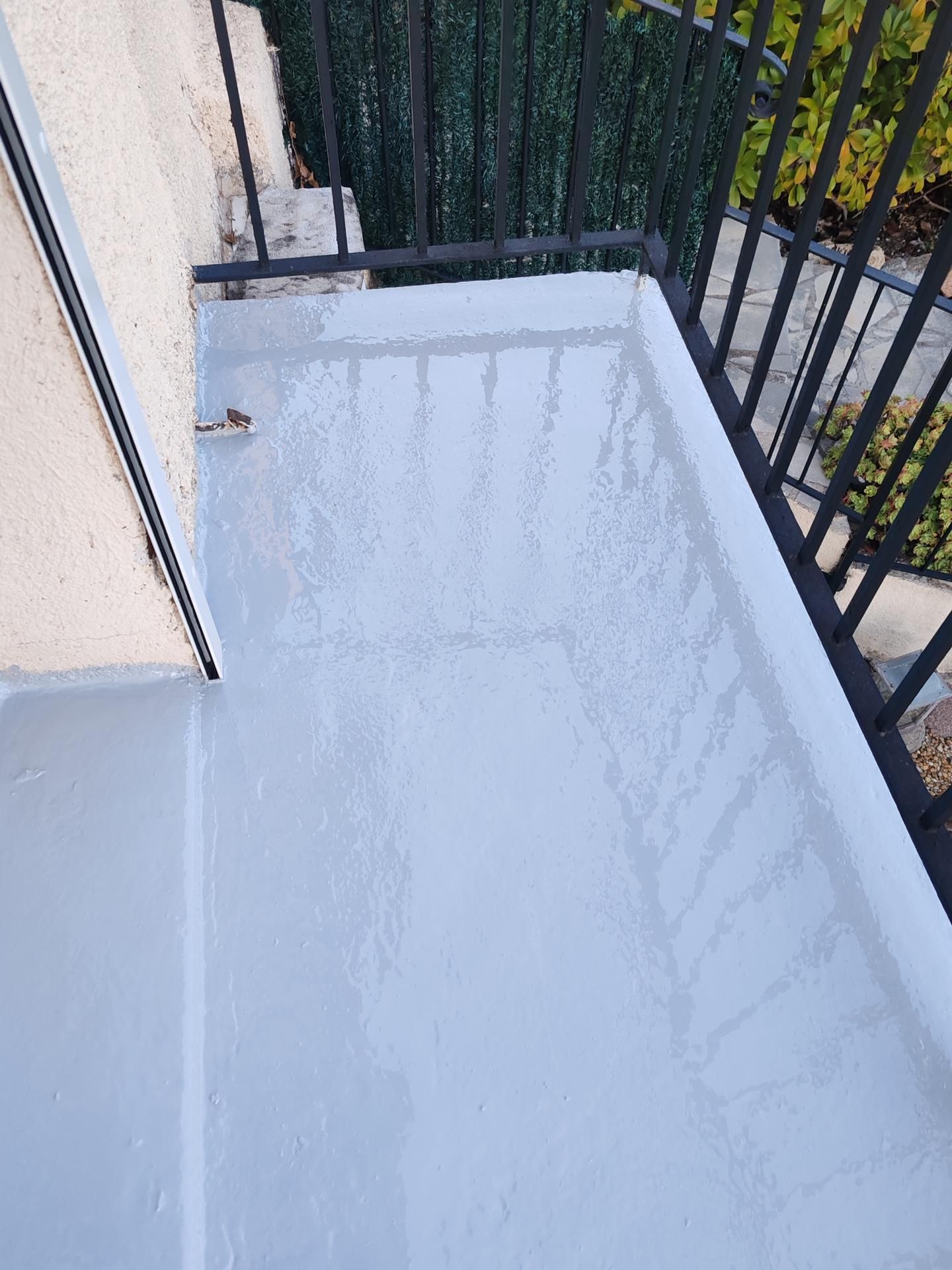 Un balcon au sol gris fraîchement peint, avec une rambarde en métal noir donnant sur la verdure.