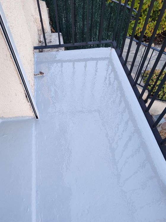 Un balcon au sol gris fraîchement peint, avec une rambarde en métal noir donnant sur la verdure.